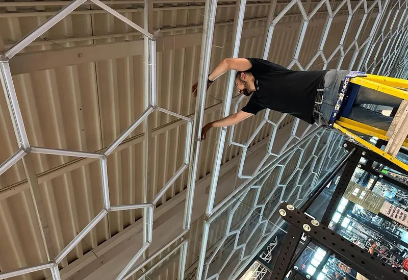 A Two Lions electrician on a ladder in a commercial space, working at the angular ceiling grid — their own photograph.