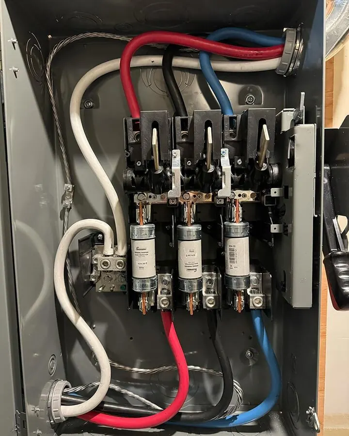An open fused disconnect with the cartridge fuses seated and the conductors landed and dressed — Two Lions' own photograph.