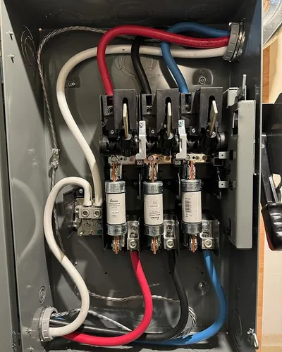 A close crop of an open fused disconnect, cartridge fuses seated in their clips and the line and load conductors landed and dressed.